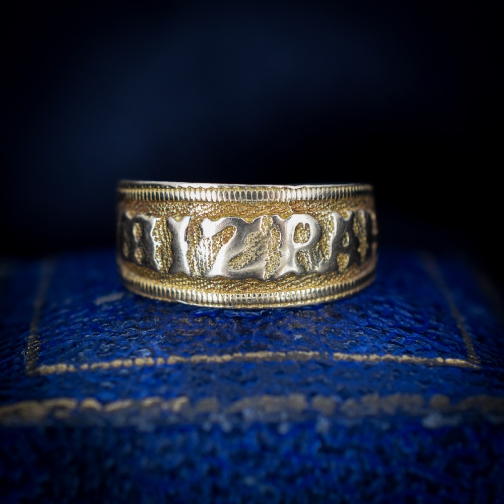 A wide yellow gold band ring featuring raised lettering spelling MIZPAH against a textured background with milled borders.