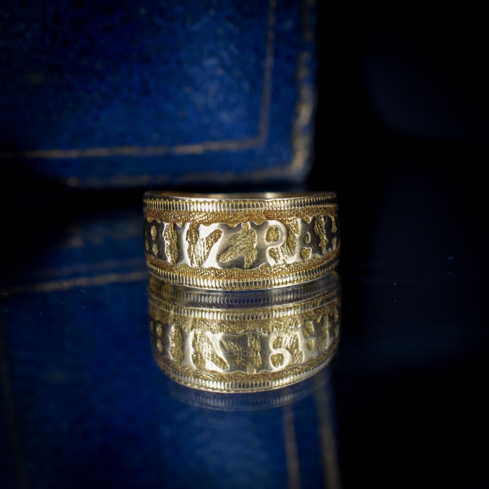 A wide yellow gold band ring featuring raised lettering spelling MIZPAH against a textured background with milled borders. View II