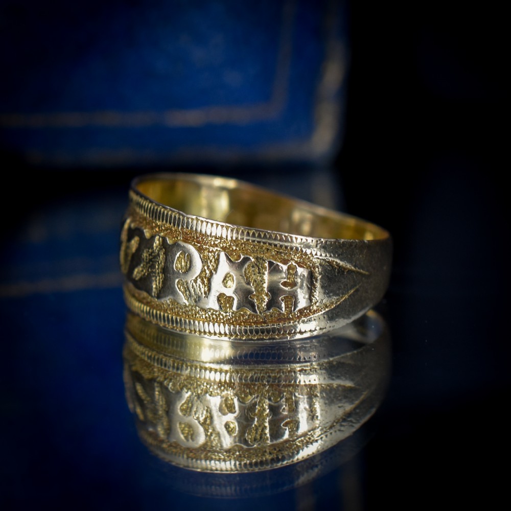 A wide yellow gold band ring featuring raised lettering spelling MIZPAH against a textured background with milled borders. View IV