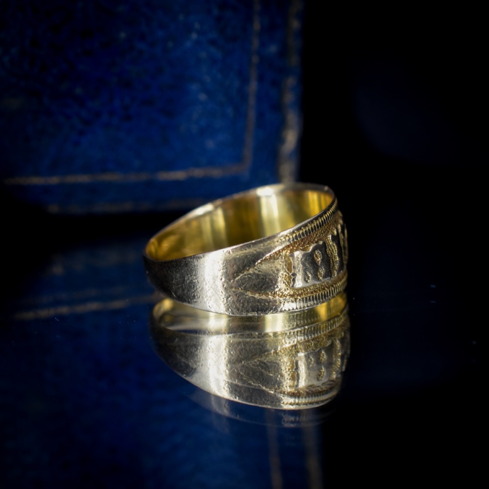 A wide yellow gold band ring featuring raised lettering spelling MIZPAH against a textured background with milled borders. View VI