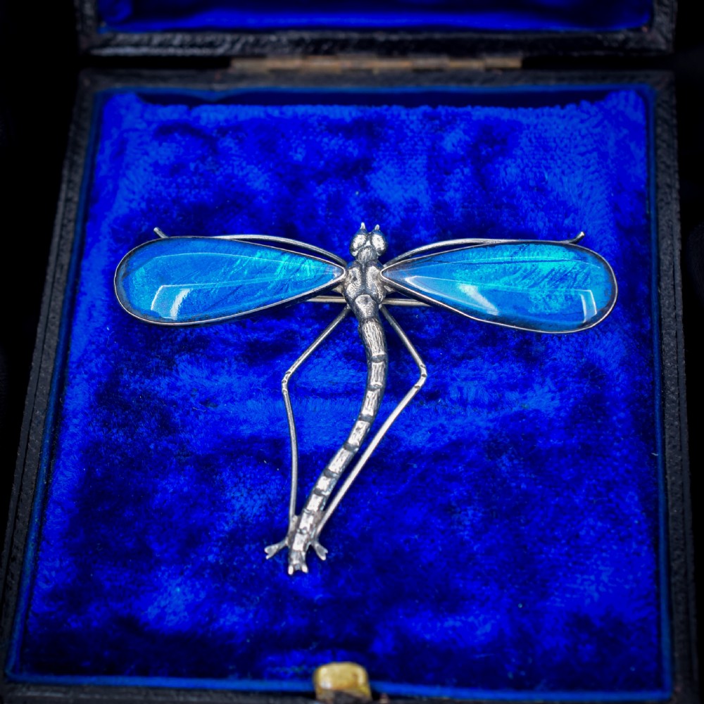 An Art Deco sterling silver brooch designed in the shape of a dragonfly with iridescent blue butterfly wings set beneath glass.