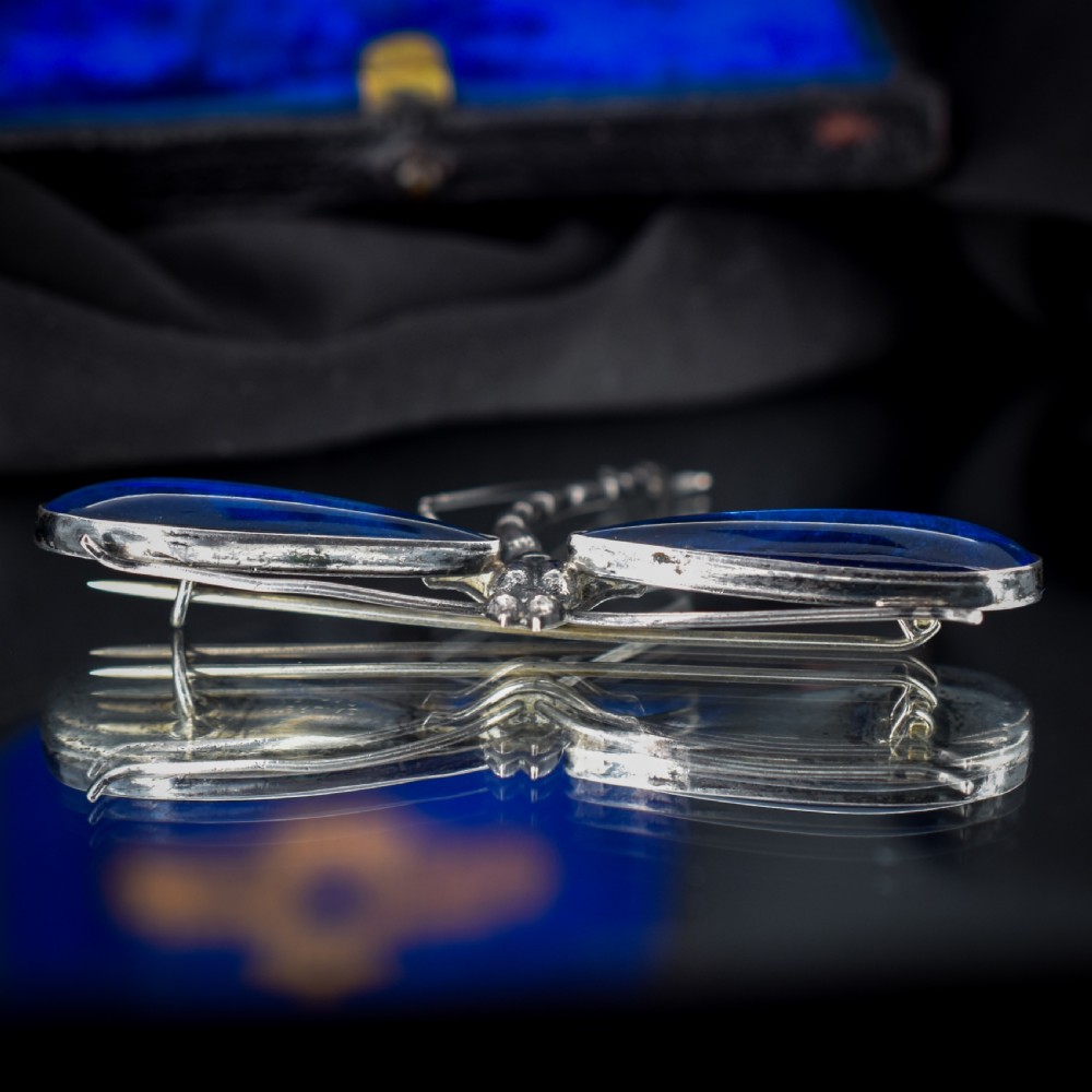 An Art Deco sterling silver brooch designed in the shape of a dragonfly with iridescent blue butterfly wings set beneath glass. View VI