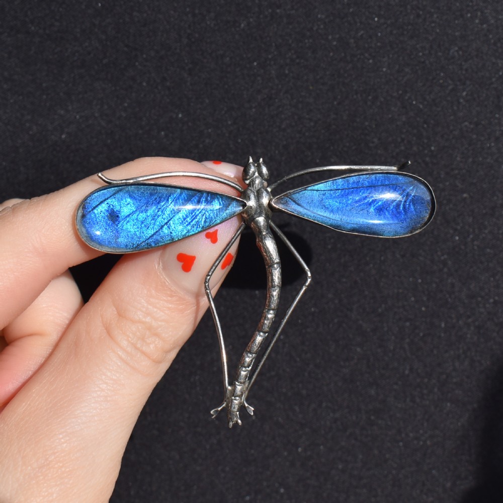 An Art Deco sterling silver brooch designed in the shape of a dragonfly with iridescent blue butterfly wings set beneath glass. View VIII