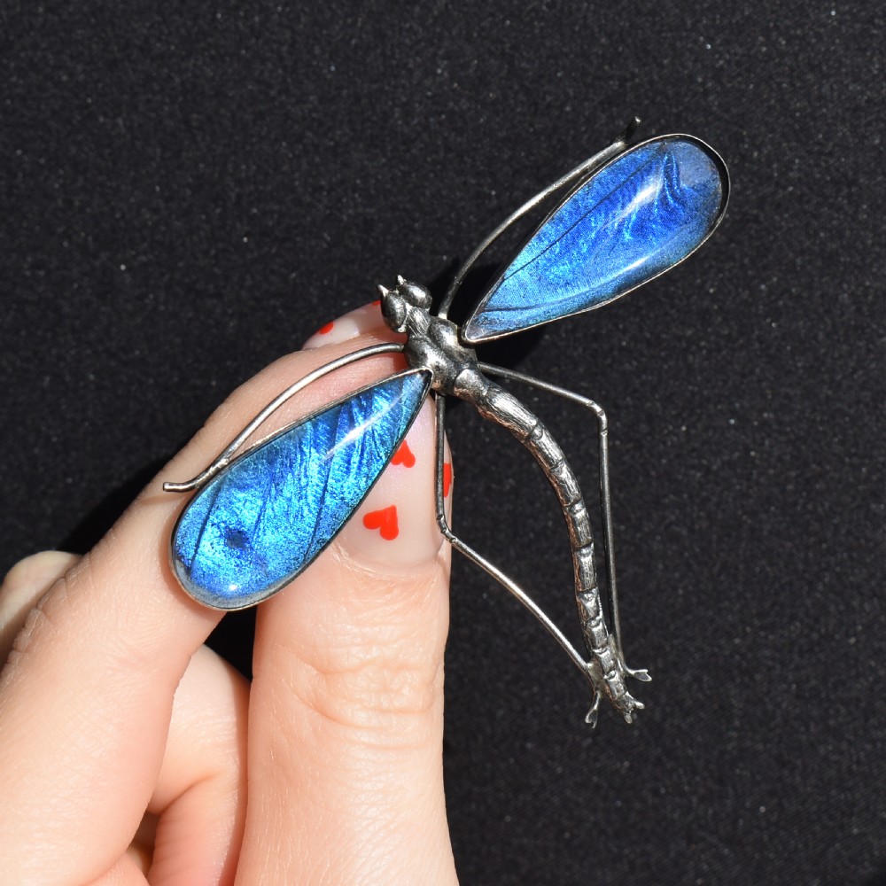 An Art Deco sterling silver brooch designed in the shape of a dragonfly with iridescent blue butterfly wings set beneath glass. View IX
