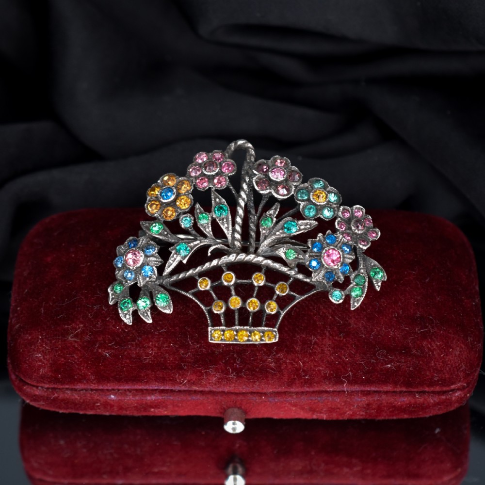 An openwork silver brooch crafted in the shape of a flower basket, set with round multi-coloured paste stones in pink, blue, yellow, and green.