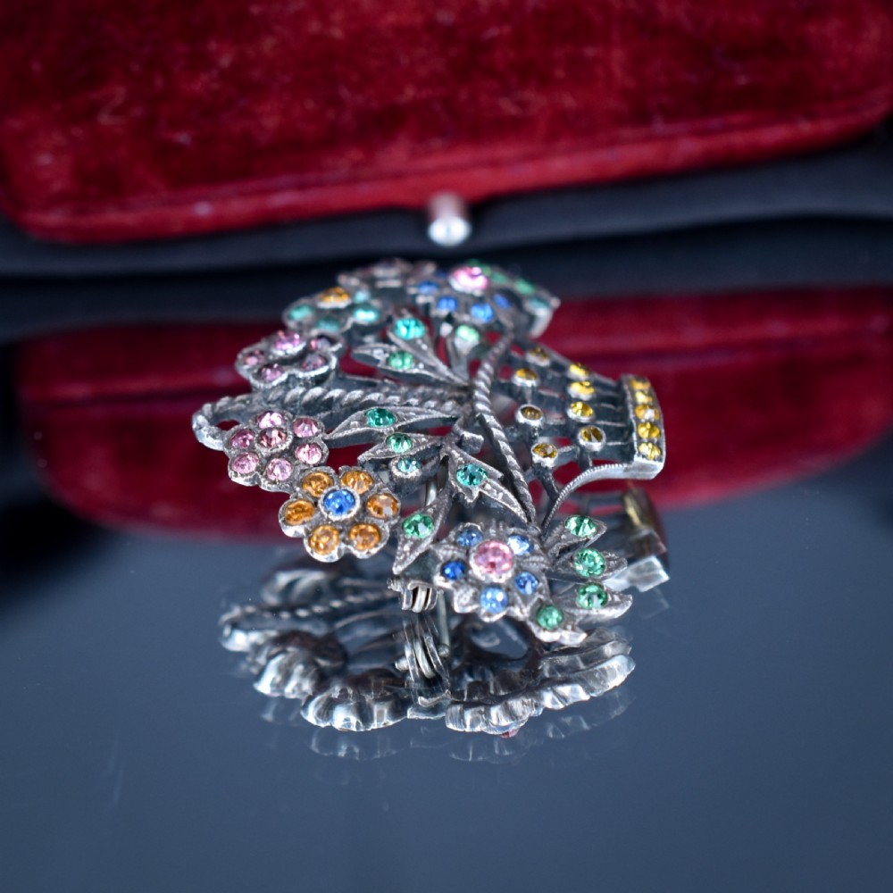 An openwork silver brooch crafted in the shape of a flower basket, set with round multi-coloured paste stones in pink, blue, yellow, and green. View II