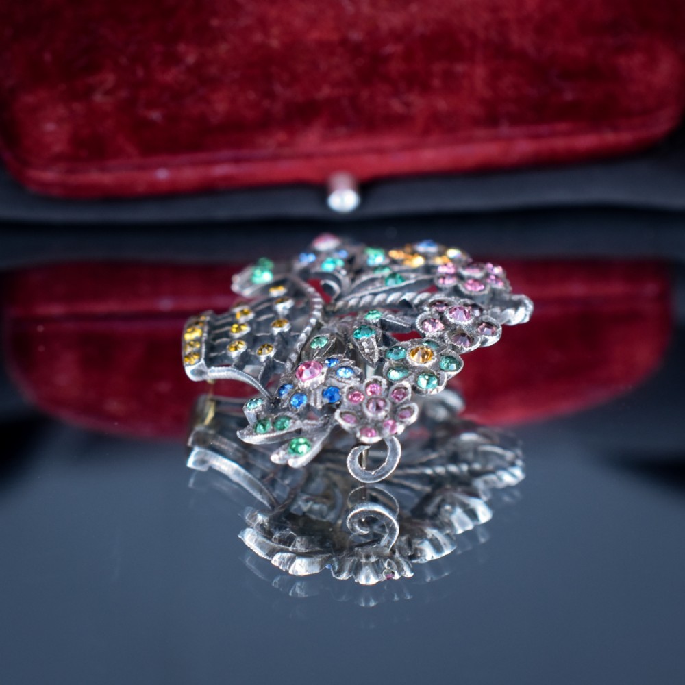 An openwork silver brooch crafted in the shape of a flower basket, set with round multi-coloured paste stones in pink, blue, yellow, and green. View IV