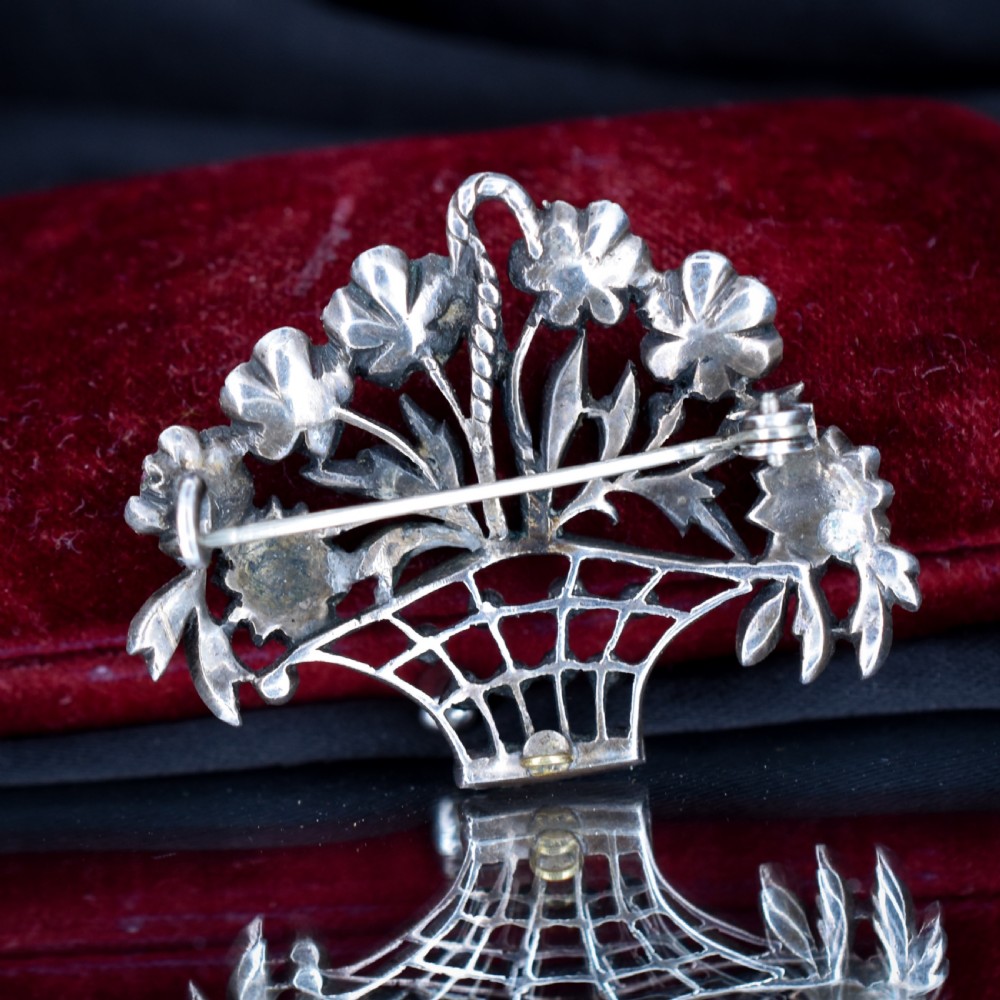 An openwork silver brooch crafted in the shape of a flower basket, set with round multi-coloured paste stones in pink, blue, yellow, and green. View V