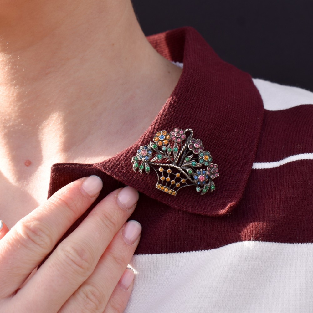 An openwork silver brooch crafted in the shape of a flower basket, set with round multi-coloured paste stones in pink, blue, yellow, and green. View VIII
