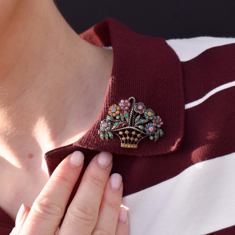 An openwork silver brooch crafted in the shape of a flower basket, set with round multi-coloured paste stones in pink, blue, yellow, and green. View IX