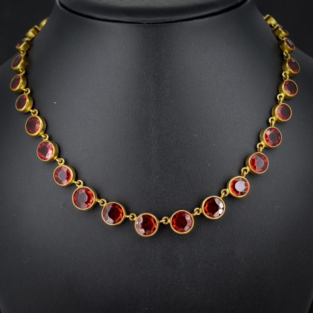 An Edwardian gold gilt riviere necklace featuring round, bezel-set facetted red paste stones connected by fine metal links.