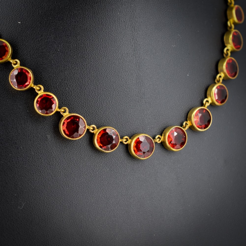 An Edwardian gold gilt riviere necklace featuring round, bezel-set facetted red paste stones connected by fine metal links. View II
