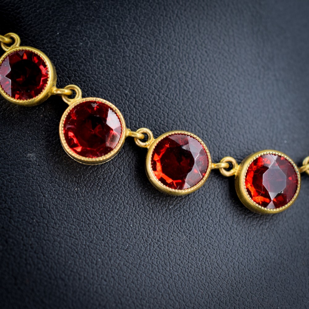 An Edwardian gold gilt riviere necklace featuring round, bezel-set facetted red paste stones connected by fine metal links. View III
