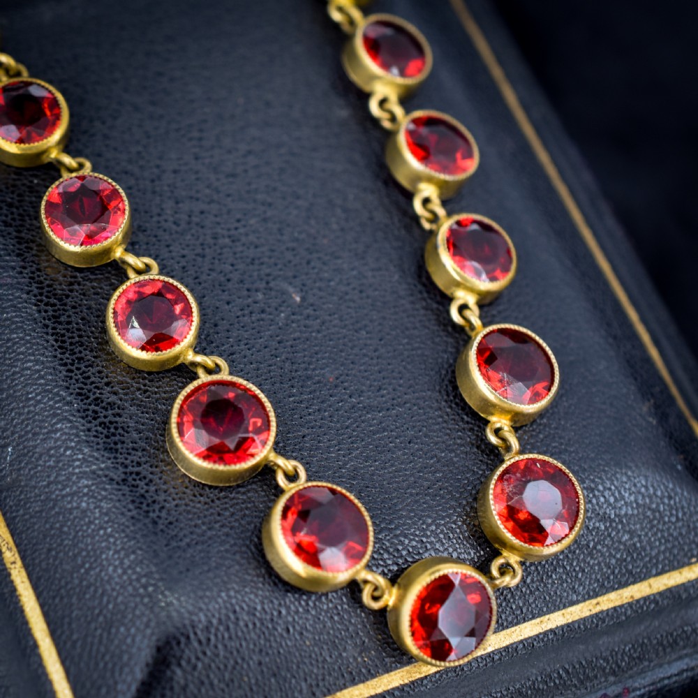 An Edwardian gold gilt riviere necklace featuring round, bezel-set facetted red paste stones connected by fine metal links. View IV