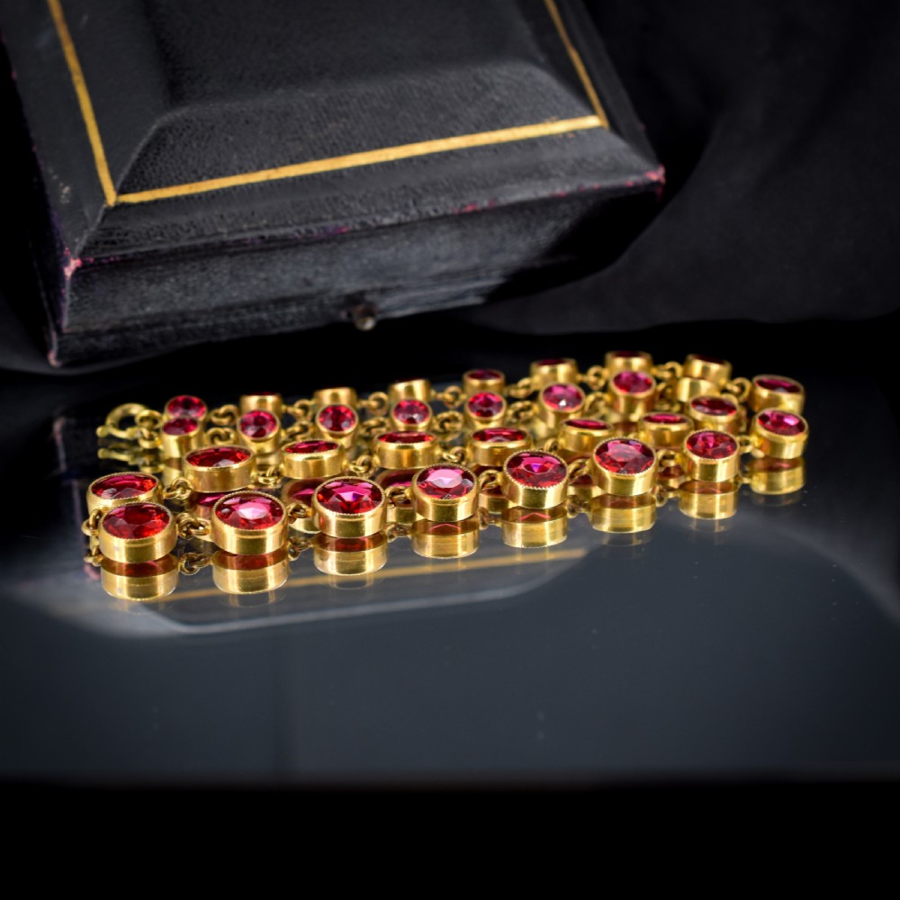 An Edwardian gold gilt riviere necklace featuring round, bezel-set facetted red paste stones connected by fine metal links. View V