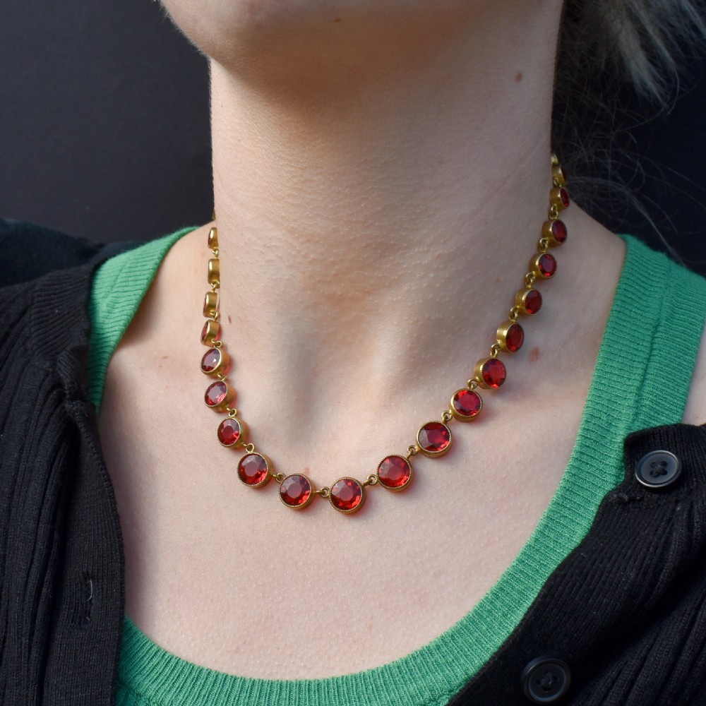 An Edwardian gold gilt riviere necklace featuring round, bezel-set facetted red paste stones connected by fine metal links. View VIII