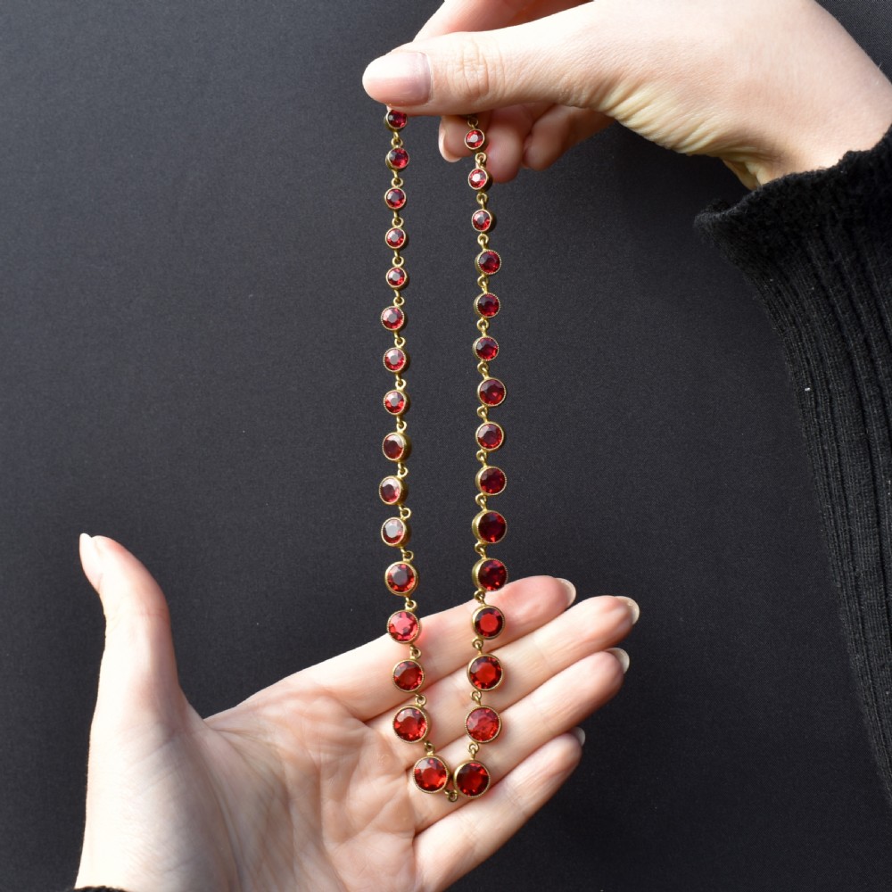 An Edwardian gold gilt riviere necklace featuring round, bezel-set facetted red paste stones connected by fine metal links. View IX