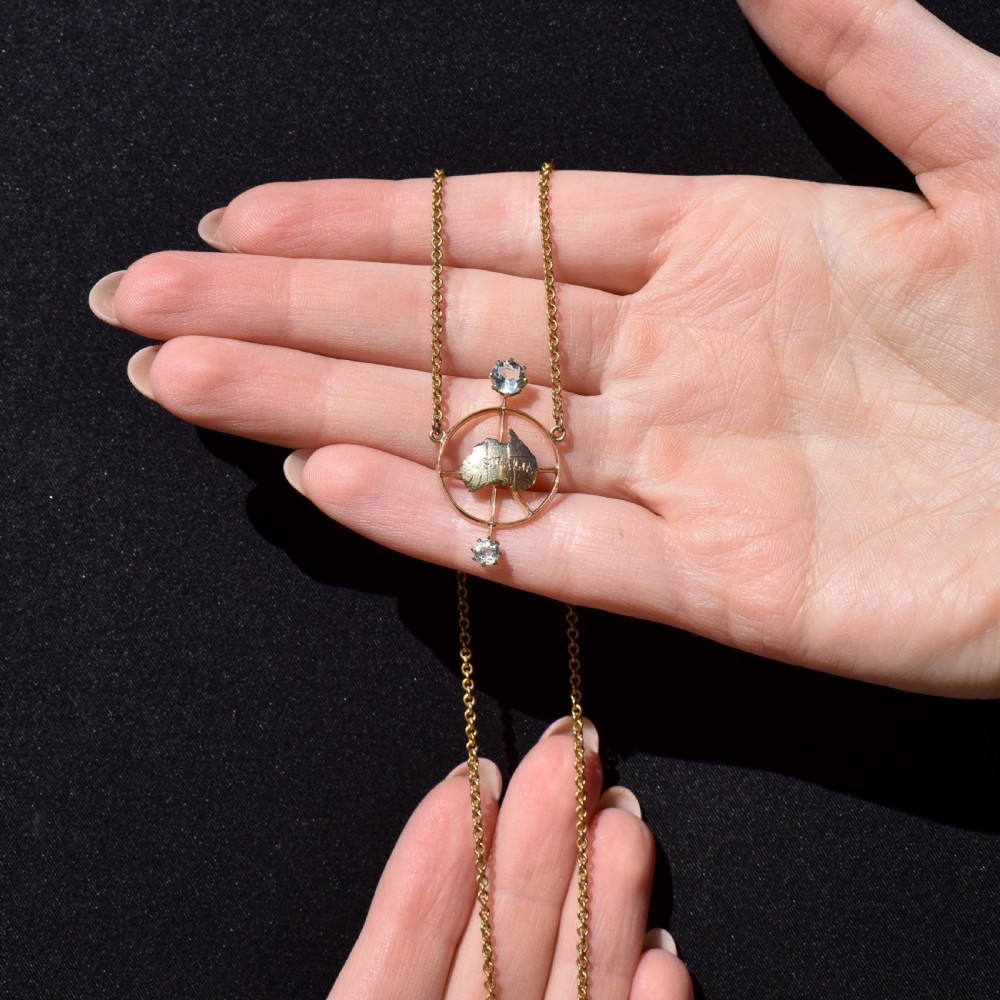 A 15ct yellow gold chain supporting a circular drop pendant featuring an Australian continent map cutout set between two round paste stones. View X