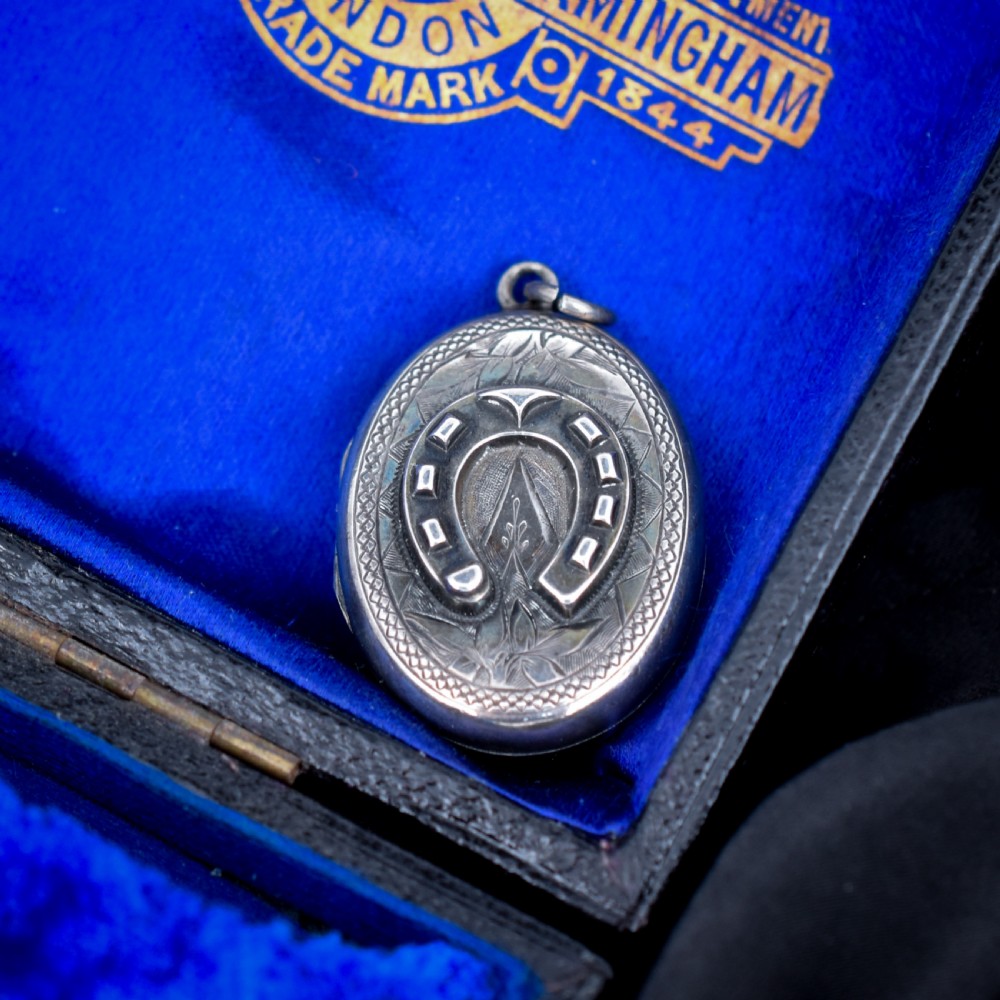 An oval antique sterling silver locket decorated with an applied horseshoe motif and hand-engraved leaf patterns.