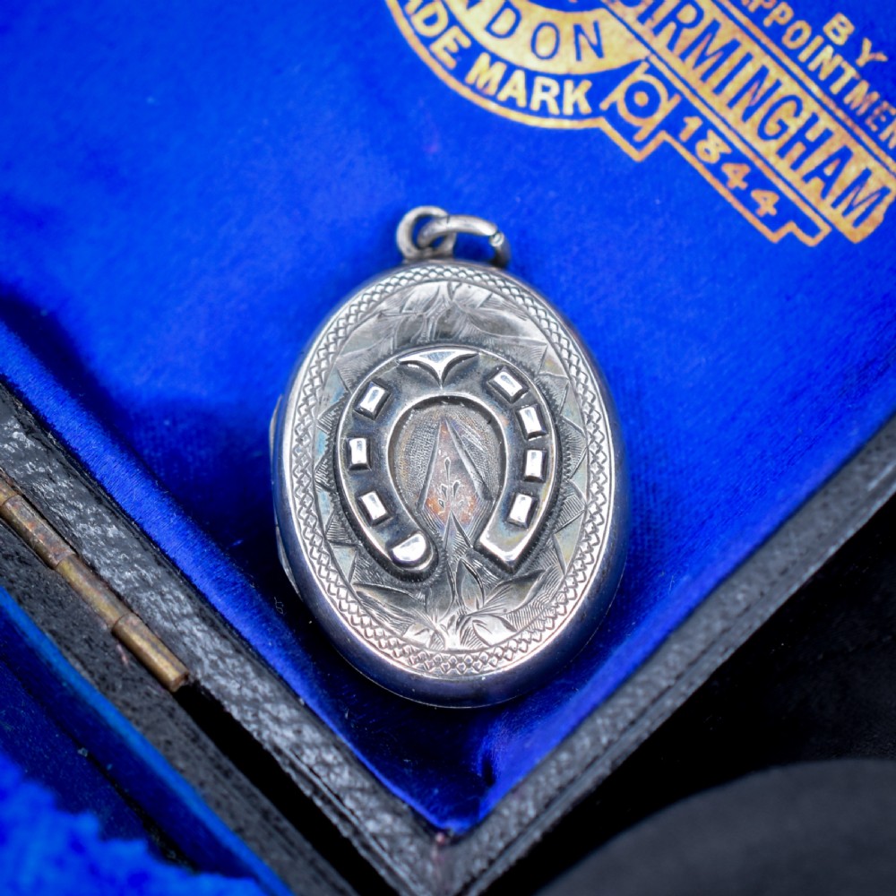 An oval antique sterling silver locket decorated with an applied horseshoe motif and hand-engraved leaf patterns. View II