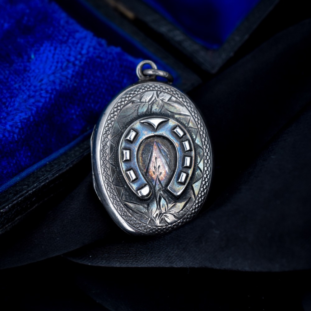 An oval antique sterling silver locket decorated with an applied horseshoe motif and hand-engraved leaf patterns. View III