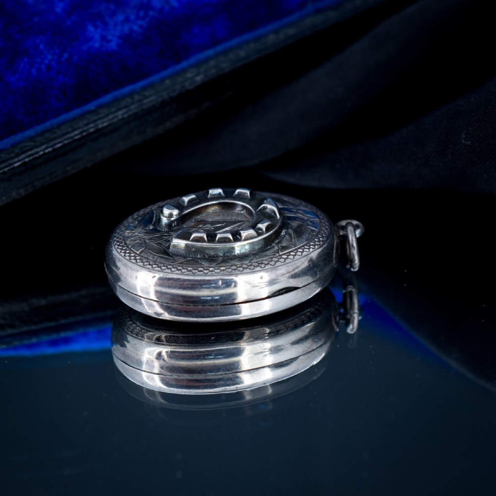 An oval antique sterling silver locket decorated with an applied horseshoe motif and hand-engraved leaf patterns. View IV