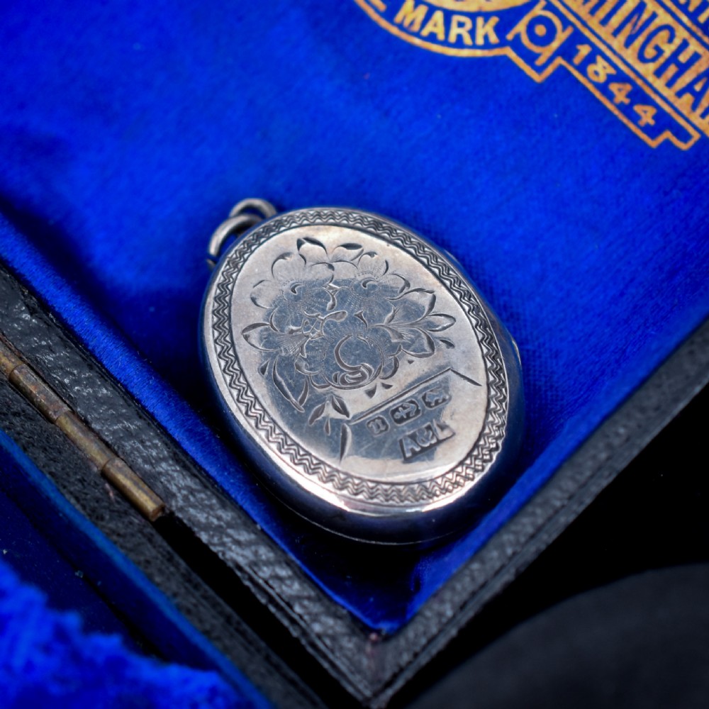 An oval antique sterling silver locket decorated with an applied horseshoe motif and hand-engraved leaf patterns. View V