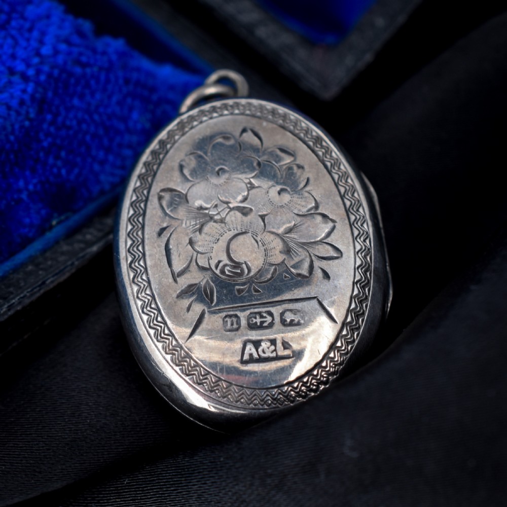 An oval antique sterling silver locket decorated with an applied horseshoe motif and hand-engraved leaf patterns. View VI