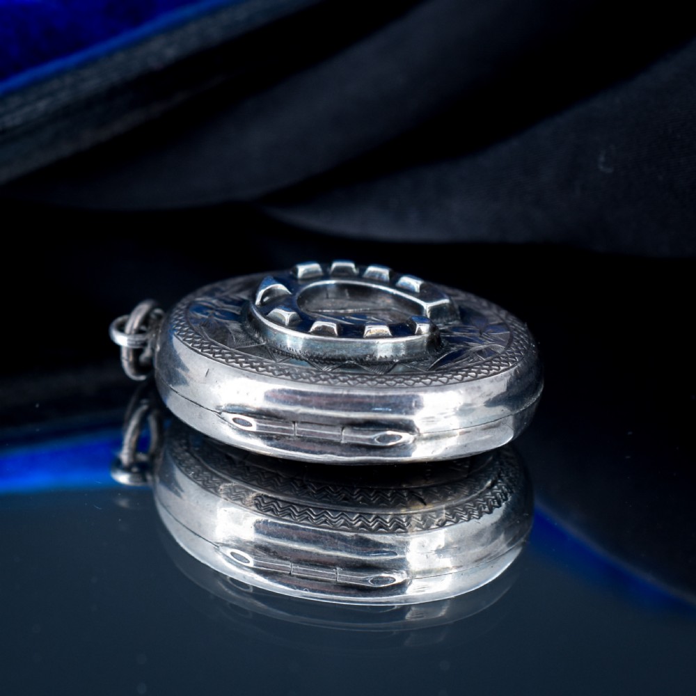 An oval antique sterling silver locket decorated with an applied horseshoe motif and hand-engraved leaf patterns. View VII