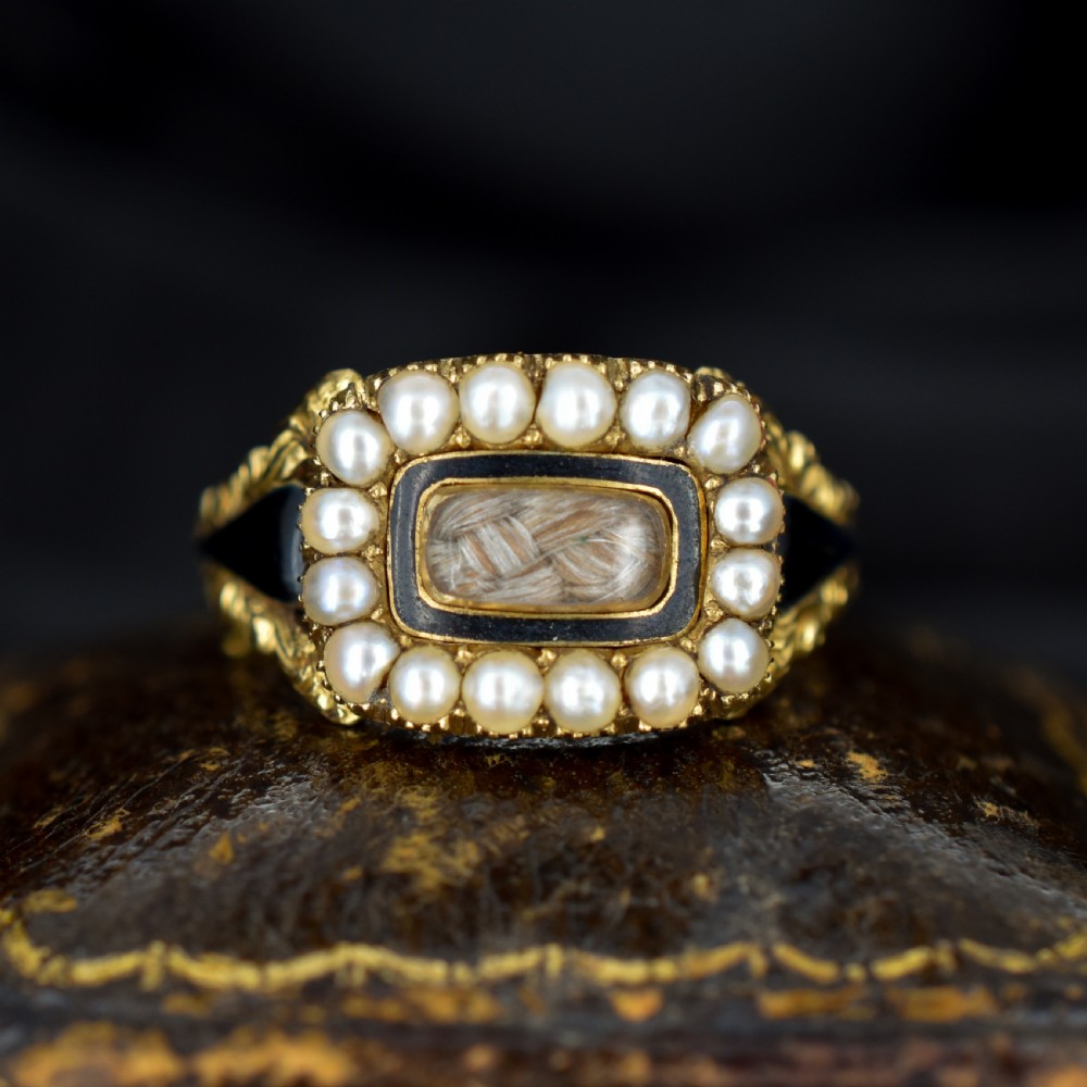 An antique 18ct gold Georgian mourning ring featuring a central woven hair compartment framed by black enamel and a border of seed pearls.