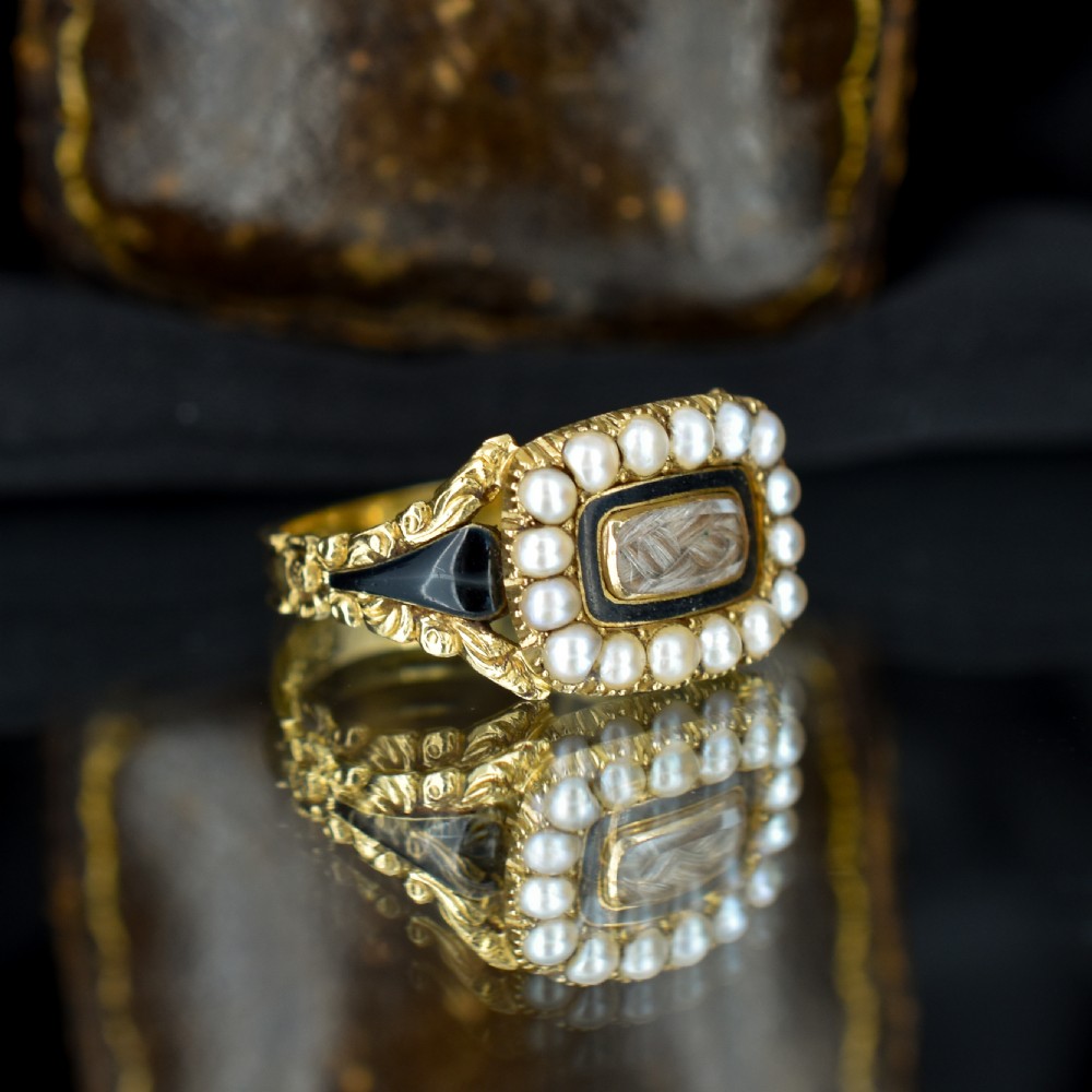 An antique 18ct gold Georgian mourning ring featuring a central woven hair compartment framed by black enamel and a border of seed pearls. View IV