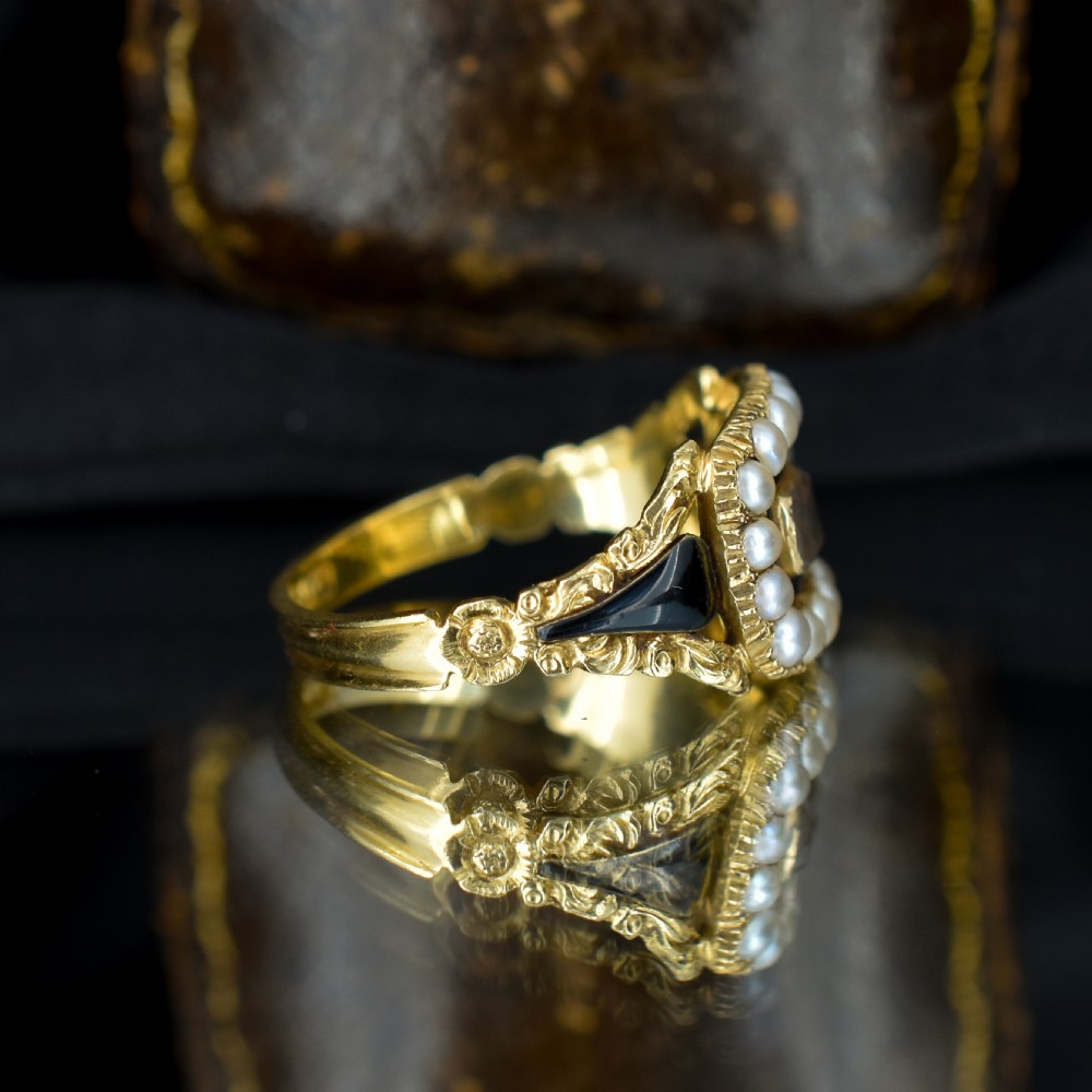 An antique 18ct gold Georgian mourning ring featuring a central woven hair compartment framed by black enamel and a border of seed pearls. View V