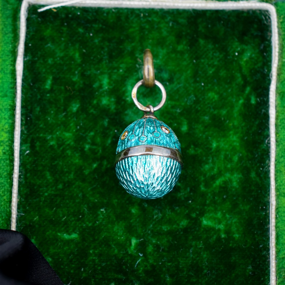 An egg-shaped silver charm pendant featuring vibrant turquoise blue guilloche enamel with fine engine-turned details and double silver mounting rings.