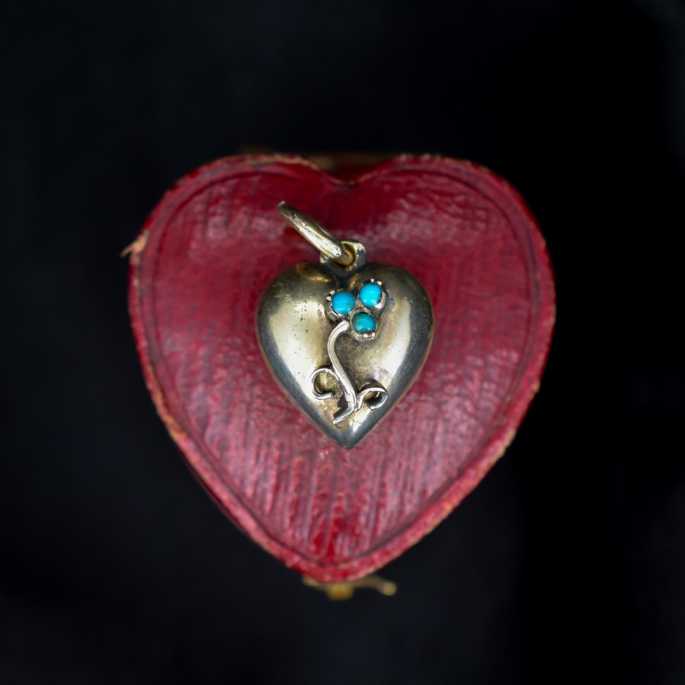 A heart-shaped gold pendant decorated with a raised stem motif set with three round blue turquoise cabochons in a floral pattern.