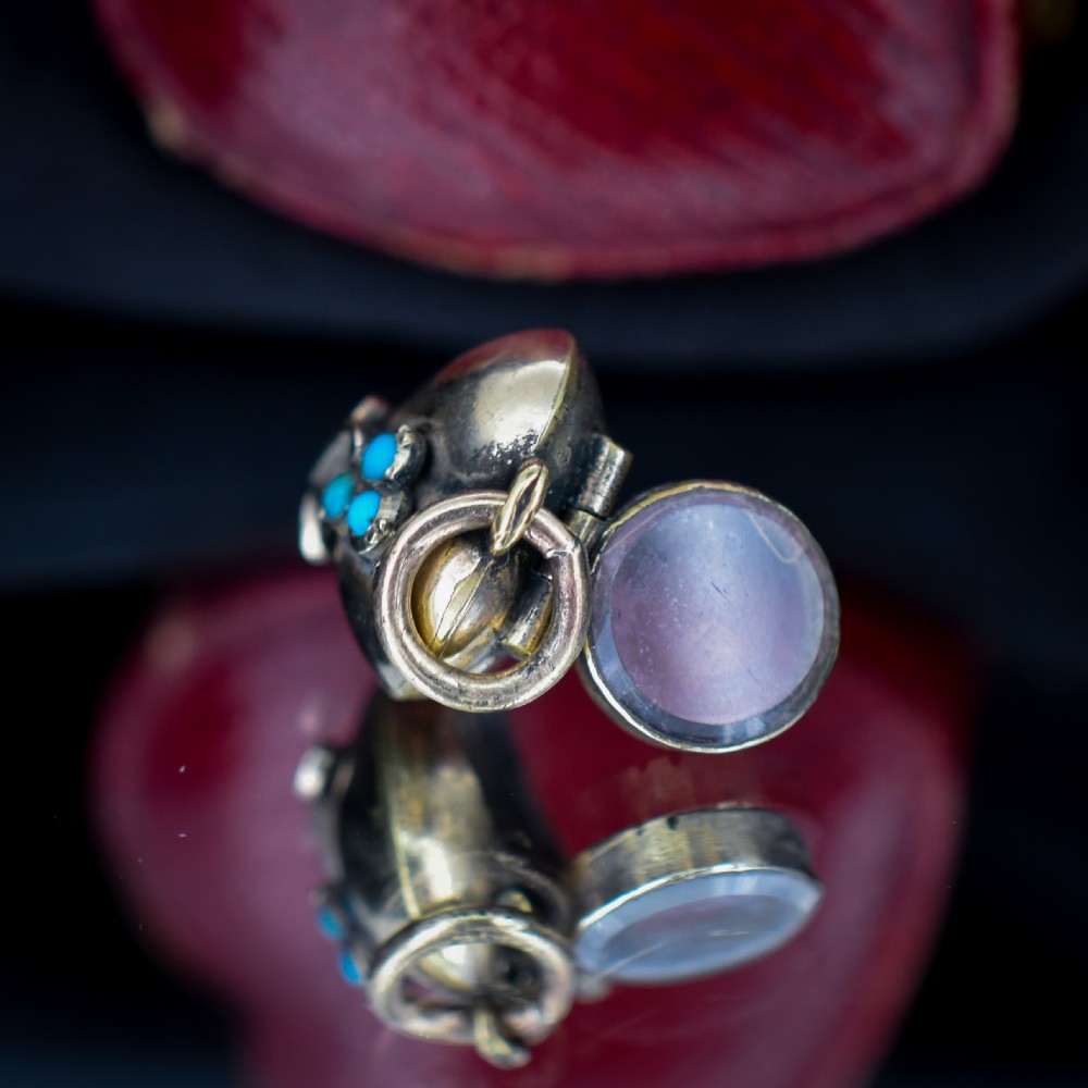 A heart-shaped gold pendant decorated with a raised stem motif set with three round blue turquoise cabochons in a floral pattern. View VI