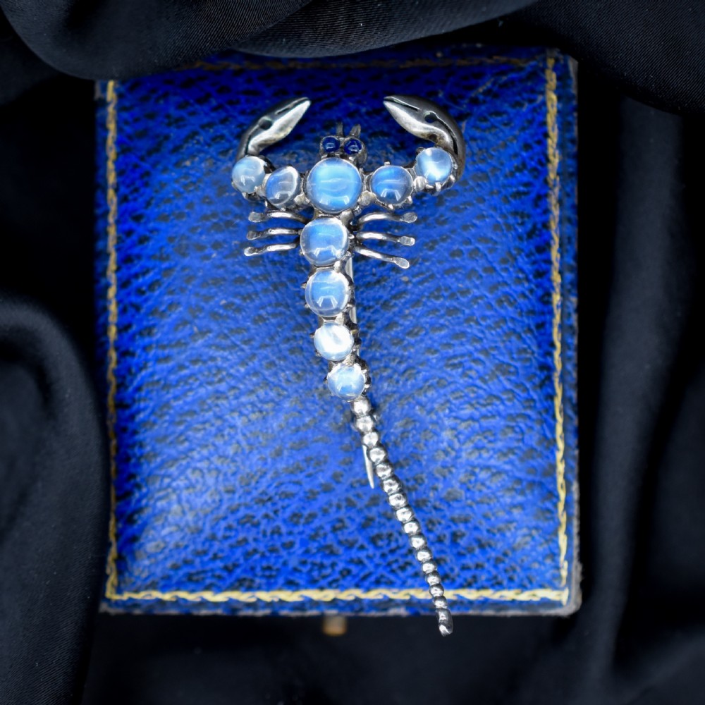 An Edwardian sterling silver brooch designed in the shape of a scorpion, featuring cabochon moonstones along its body and small blue stones for eyes.