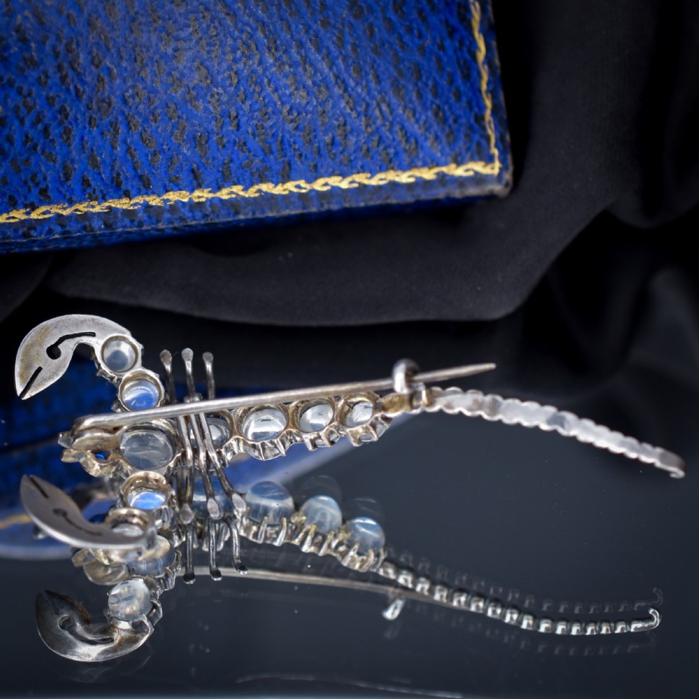 An Edwardian sterling silver brooch designed in the shape of a scorpion, featuring cabochon moonstones along its body and small blue stones for eyes. View V