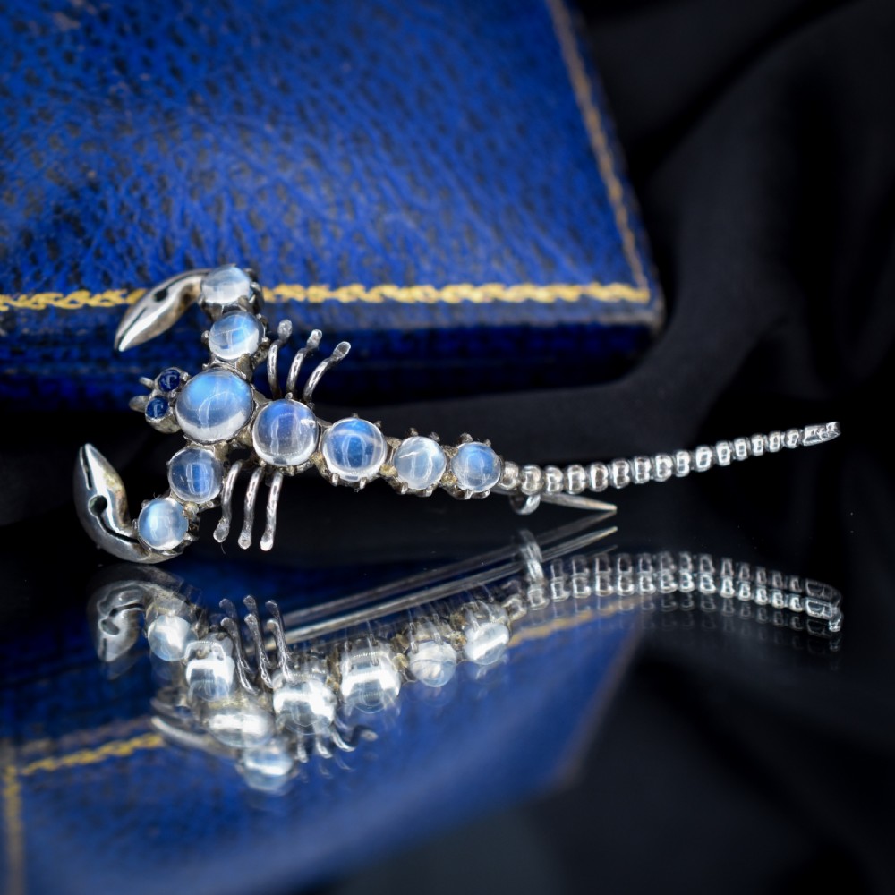 An Edwardian sterling silver brooch designed in the shape of a scorpion, featuring cabochon moonstones along its body and small blue stones for eyes. View VI
