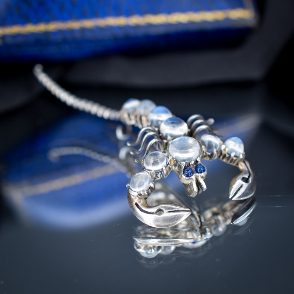 An Edwardian sterling silver brooch designed in the shape of a scorpion, featuring cabochon moonstones along its body and small blue stones for eyes. View VIII