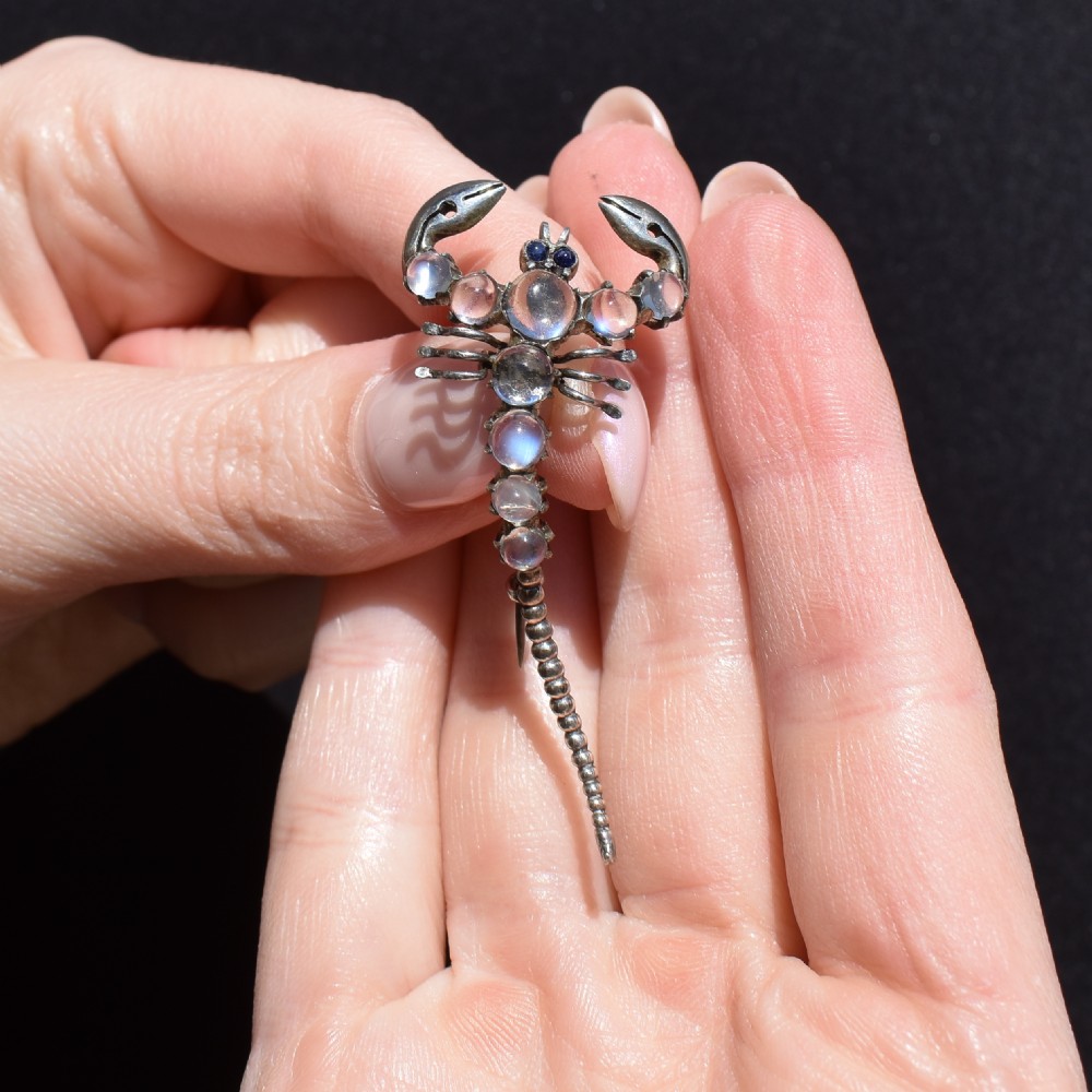 An Edwardian sterling silver brooch designed in the shape of a scorpion, featuring cabochon moonstones along its body and small blue stones for eyes. View X