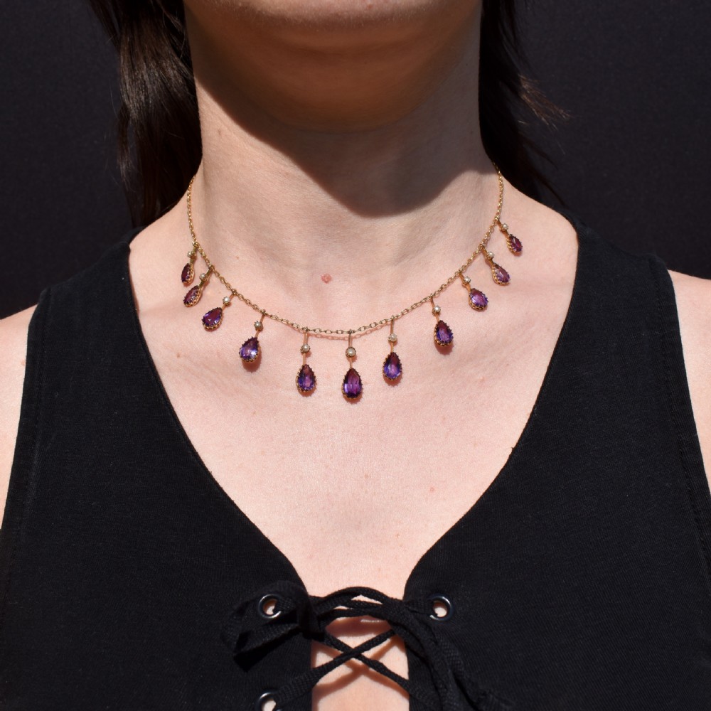 An antique gold fringe necklace featuring suspended pear-cut amethyst drops and seed pearls.