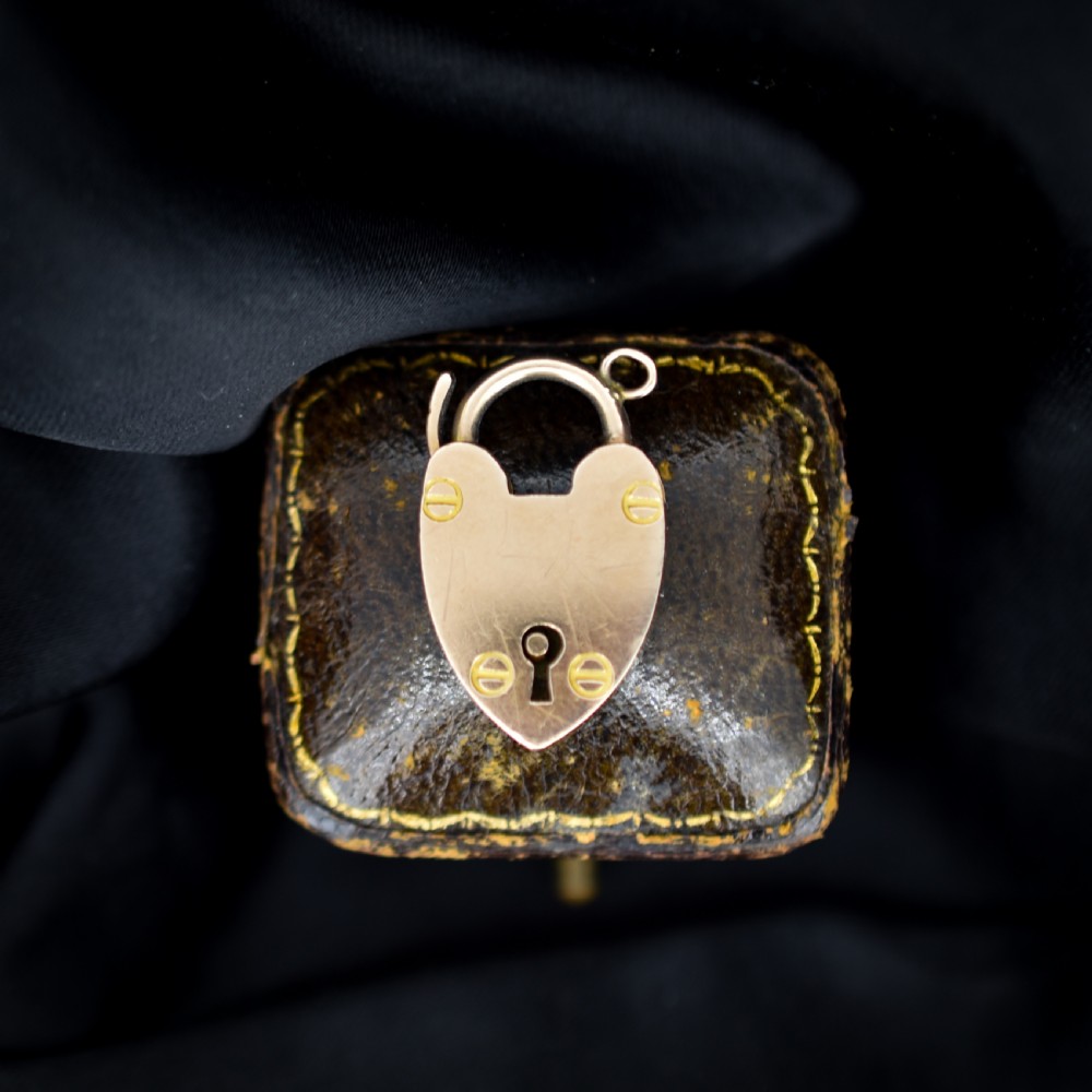 An Edwardian 9ct gold heart-shaped padlock pendant featuring four gold screw accents, a central keyhole, a top shackle catch, and a jump ring.