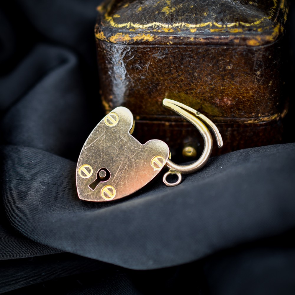 An Edwardian 9ct gold heart-shaped padlock pendant featuring four gold screw accents, a central keyhole, a top shackle catch, and a jump ring. View III