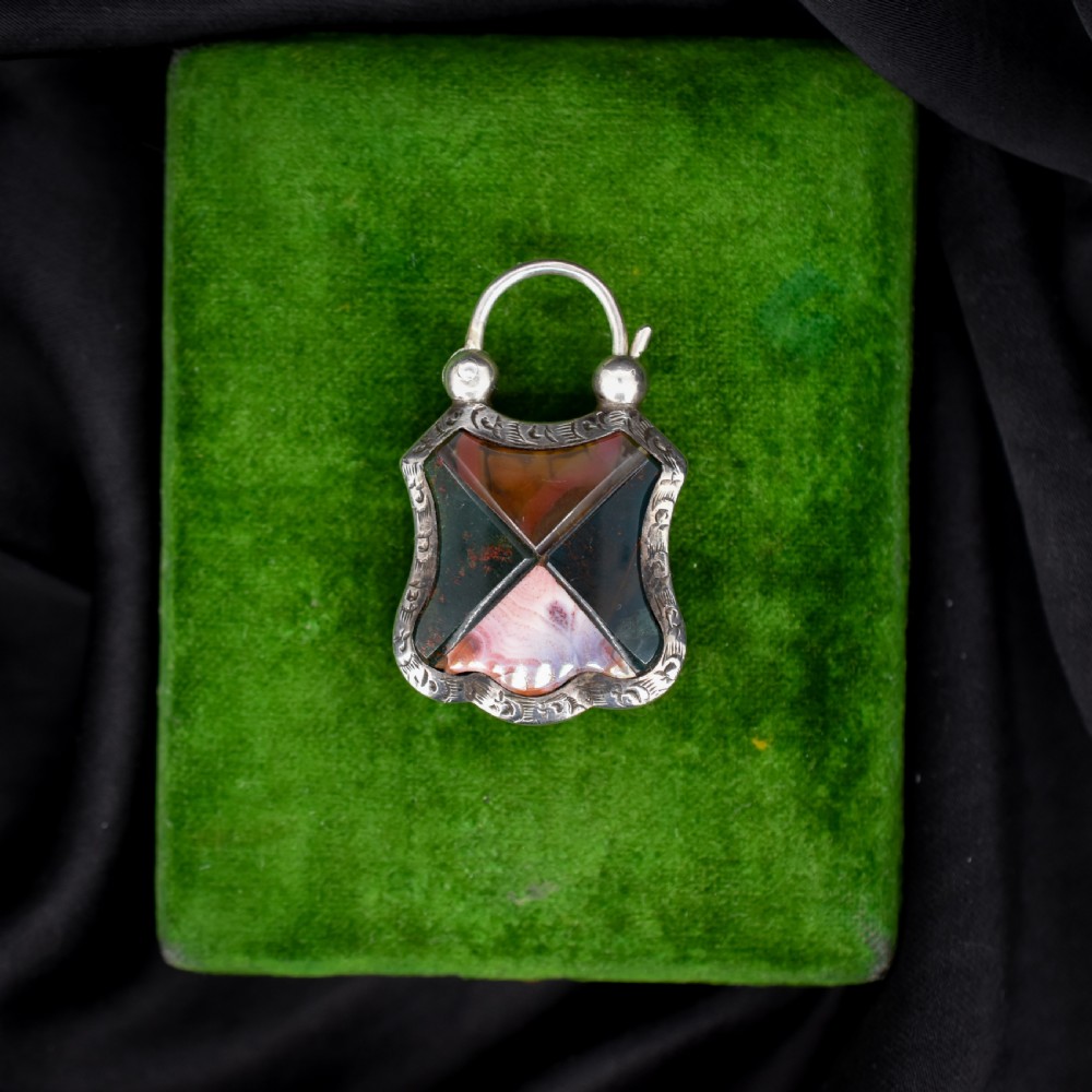 A Victorian silver padlock-shaped pendant featuring inlaid segments of red, green, and patterned agate with hand-engraved floral borders.