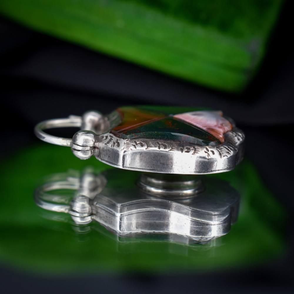 A Victorian silver padlock-shaped pendant featuring inlaid segments of red, green, and patterned agate with hand-engraved floral borders. View V