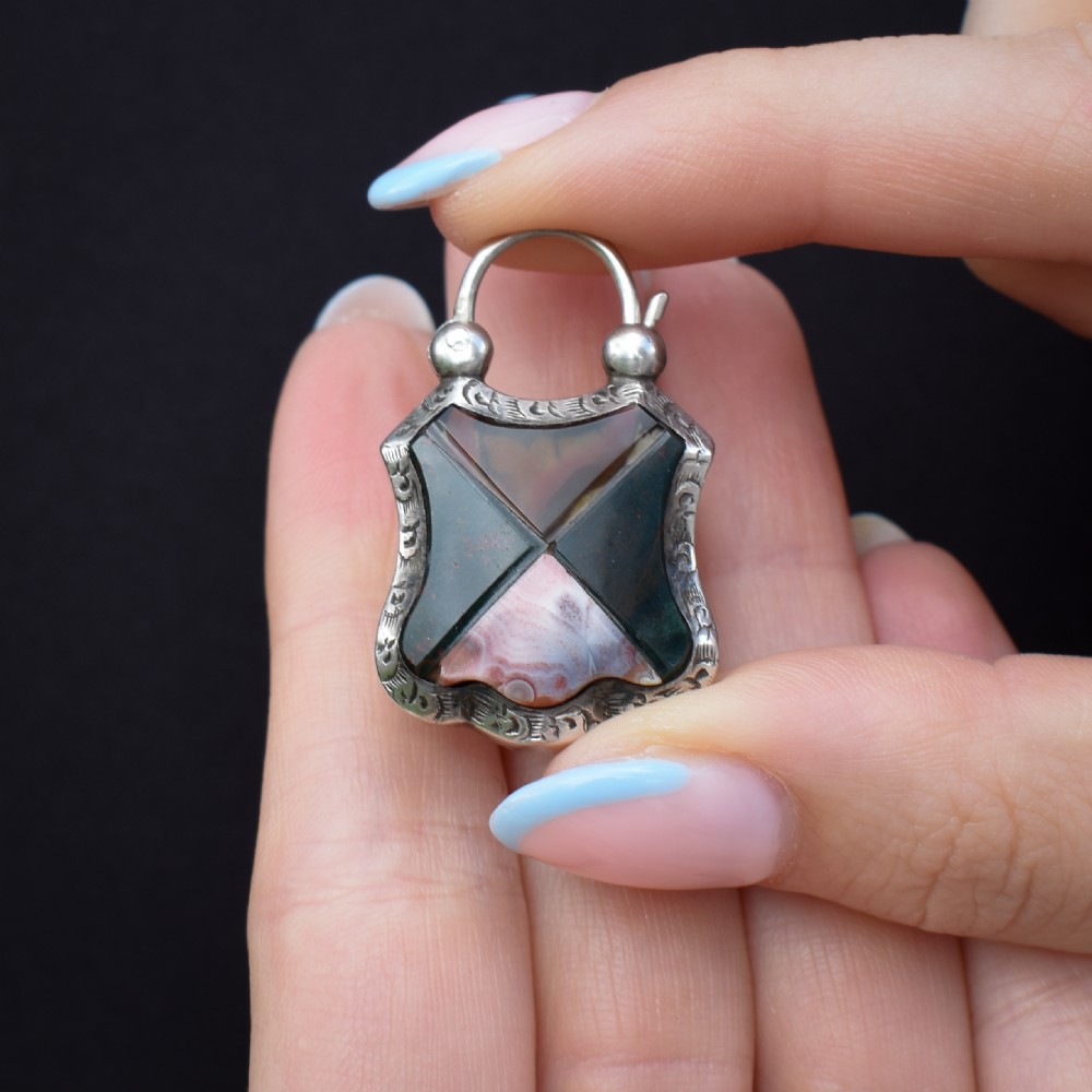 A Victorian silver padlock-shaped pendant featuring inlaid segments of red, green, and patterned agate with hand-engraved floral borders. View X