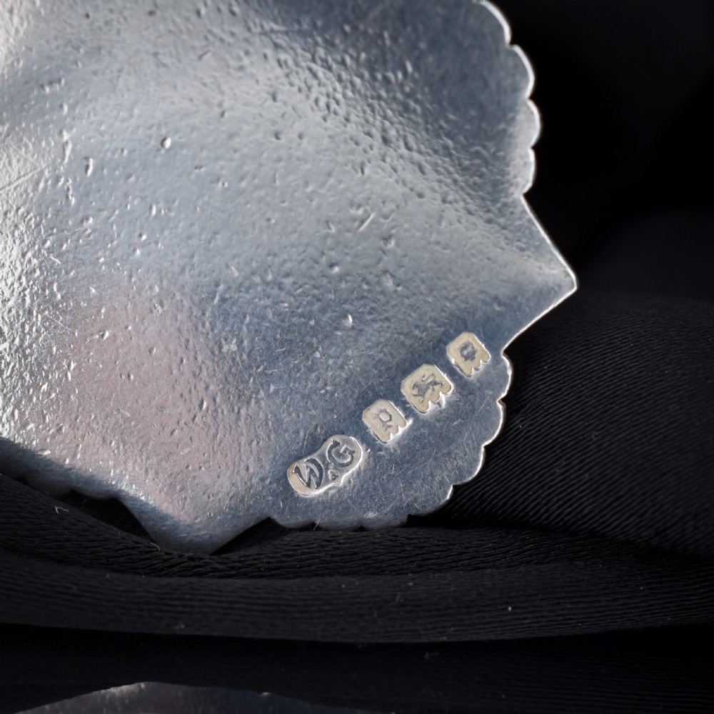 An Art Deco silver medallion featuring a central circular floral relief surrounded by a geometric square and fan-shaped fluted edges with a top suspension loop. View VI