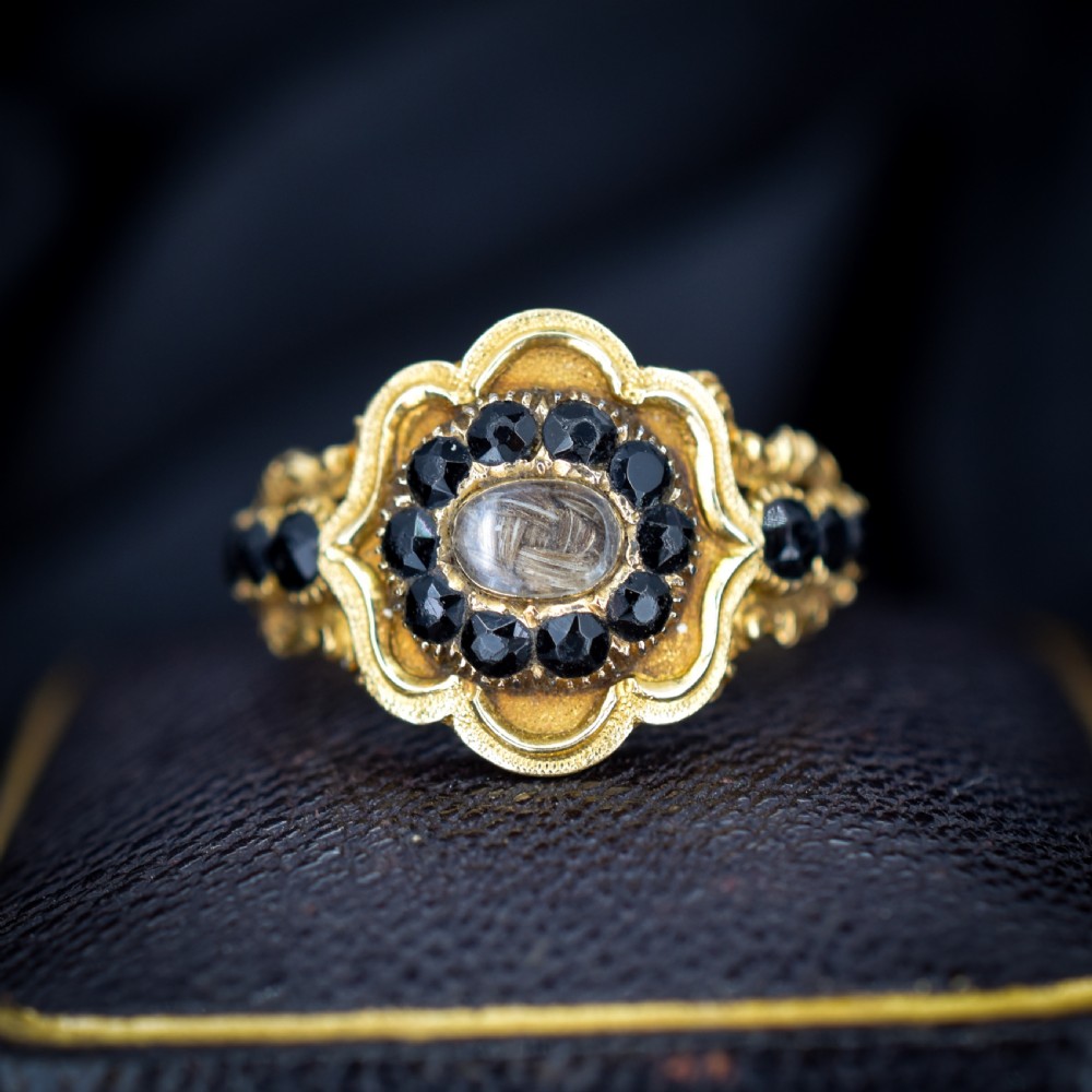 A Georgian gold ring featuring a central woven hair panel set under glass, surrounded by a cluster of faceted black jet stones.