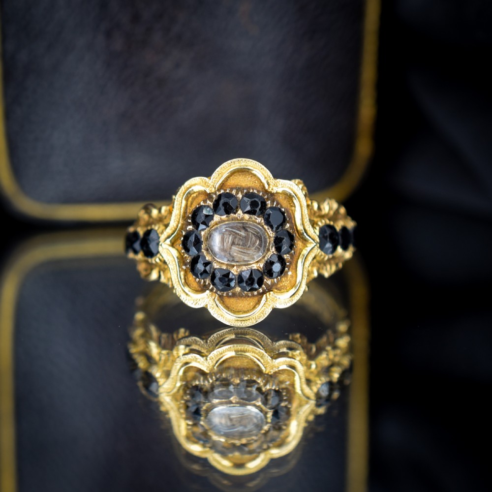 A Georgian gold ring featuring a central woven hair panel set under glass, surrounded by a cluster of faceted black jet stones. View III