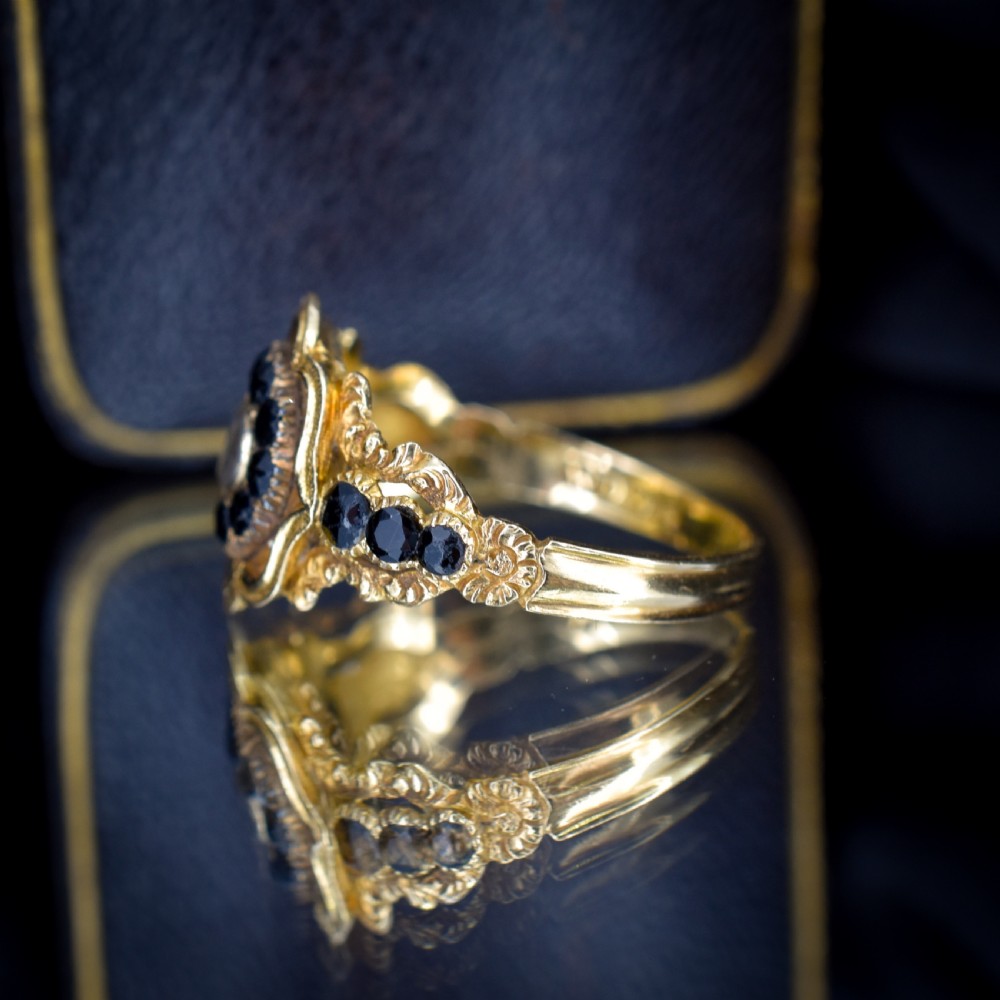 A Georgian gold ring featuring a central woven hair panel set under glass, surrounded by a cluster of faceted black jet stones. View IV